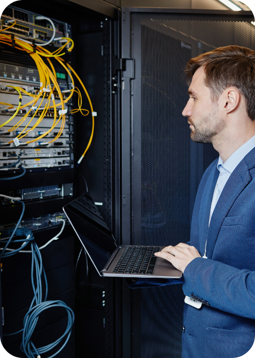 network engineer working in a server cabinet on a laptop