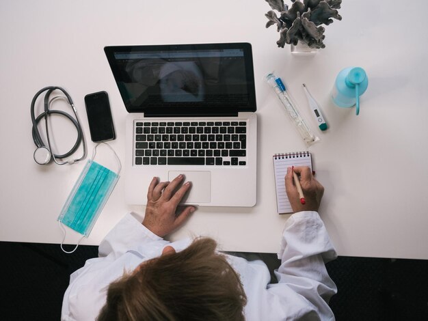 Birds eye view of healthcare worker at laptop doing work and writing notes