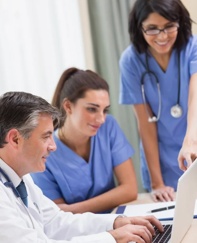 Healthcare workers gathered round a laptop sharing thoughts and smiling Healthcare workers gathered round a laptop sharing thoughts and smiling